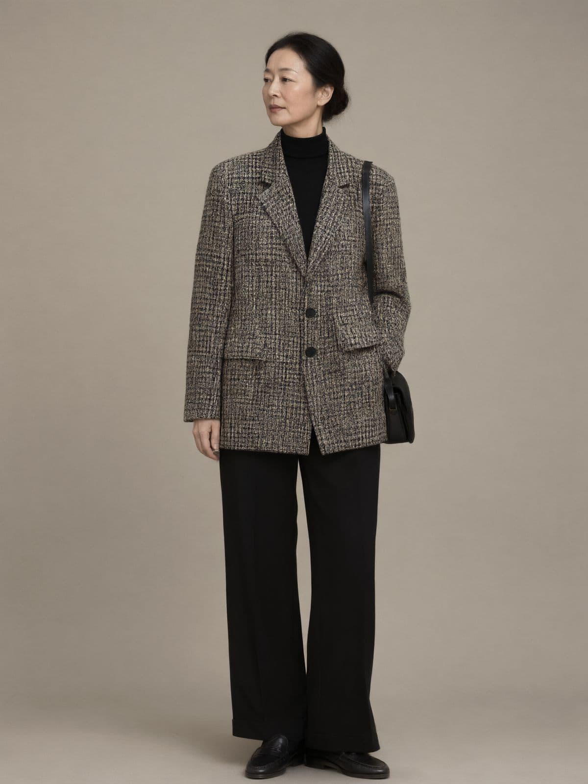 A woman wears the check blazer buttoned over a black turtleneck with black wide-leg trousers and loafers.